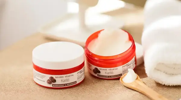 Deux pots de beurre de karité, parfaits pour les bienfaits cheveux. Une cuillère en bois en présente la texture onctueuse.
