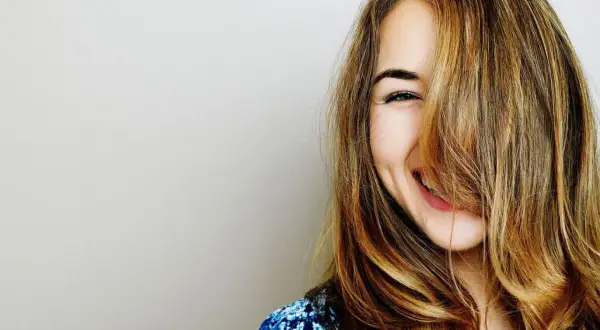 Une jeune femme rit, ses cheveux eclaircis tombant sur son visage.