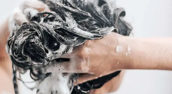 Mousse on dark, wet hair as someone is se laver les cheveux au savon de marseille.