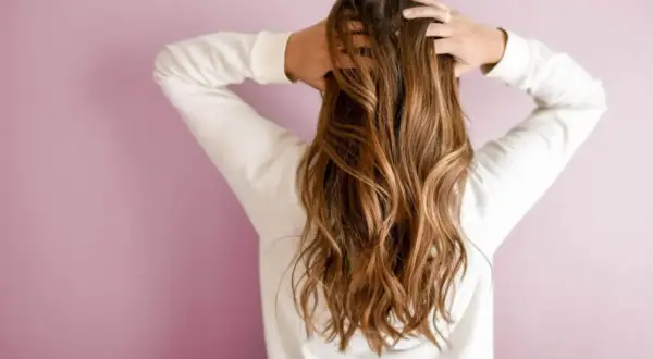 Une brune aux cheveux longs et ondulés, sublimés par un balayage caramel subtil qui capte la lumière.