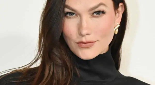 Une femme aux cheveux bruns foncés arbore une coloration claire subtile, sans décoloration visible, rehaussée par un col roulé noir et des boucles d'oreilles dorées.