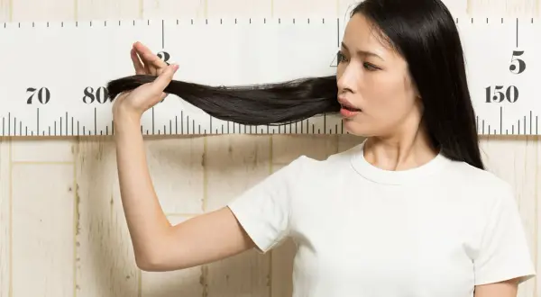 Femme mesurant sa longue chevelure noire devant une règle graduée, peut-être pour suivre le ralentir pousse cheveux.