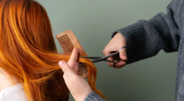 Une personne se coupe les cheveux roux avec des ciseaux, comme si elle se coupait les cheveux avec la lune.