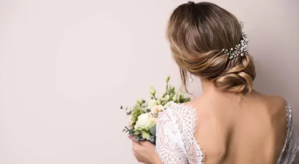 Coiffure bohème chic mi long avec un chignon bas orné de perles et de cristaux, tenant un bouquet de mariée.