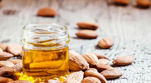 Huile d'amande dorée dans un petit pot, entourée d'amandes. Un secret naturel pour le bienfait des amandes sur les cheveux.