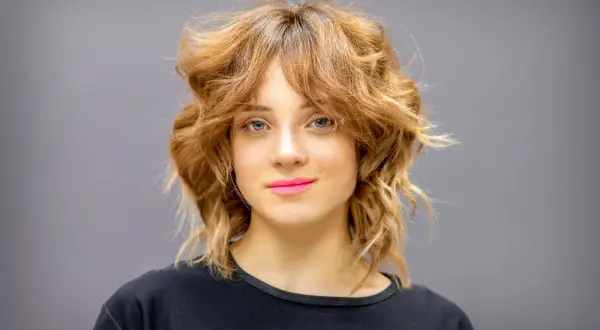 Une femme au regard bleu et aux lèvres roses arbore une coupe wolf cut dégradée et texturisée, un style audacieux et moderne.