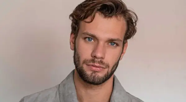 Un homme aux yeux bleus perçants arbore une coupe homme cheveux raides, légèrement ondulés sur le dessus, et une barbe courte.