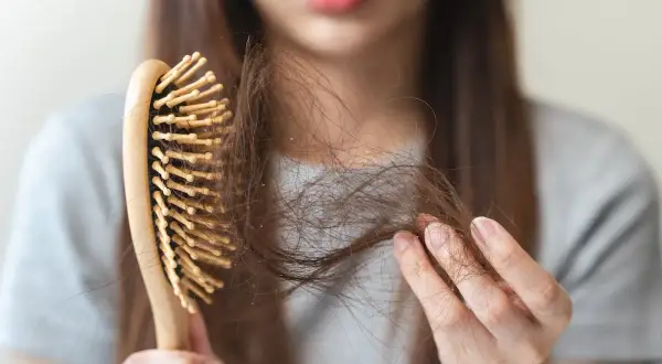 Une femme examine sa brosse à cheveux, remplie de mèches, signe de cheveux cassants.