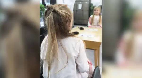 Une petite fille avec une jolie demi queue de cheval torsadée, assise à une table.