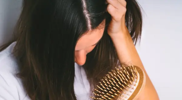 Une femme observe une brosse à cheveux remplie de cheveux, signe d'une possible chute de cheveux en automne.