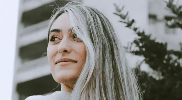 Portrait d'une jeune femme aux cheveux blonds, avec une transition grey blending subtile. Elle regarde au loin, un léger sourire aux lèvres.
