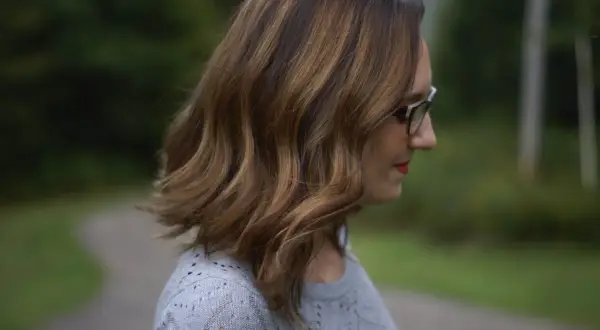 Profil d'une femme aux cheveux châtain avec des mèches blanches, portant des lunettes.