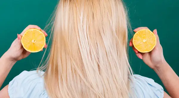 Une femme aux cheveux blonds tient des moitiés de citron près de ses oreilles, suggérant des aliments mauvais pour les cheveux.