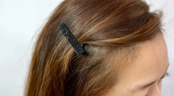 Une mèche de cheveux châtain est fixée avec une barrette noire scintillante. Une coiffure facile pour un look rapide.