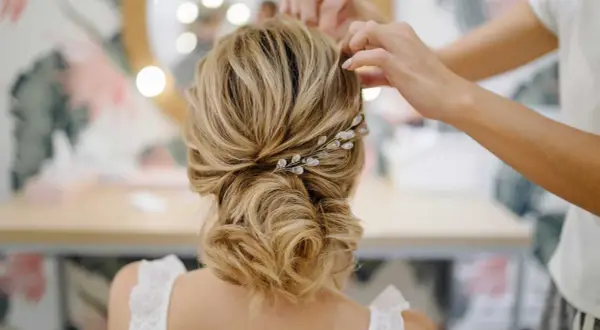 Une mariée se fait coiffer un chignon bouclé flou, orné d'une barrette scintillante.