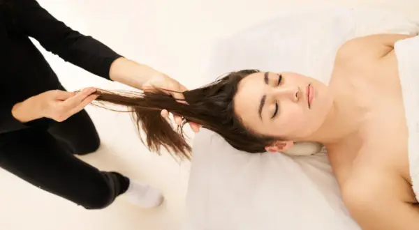 Une femme reçoit un massage du cuir chevelu pour stimuler la pousse des cheveux. Ses yeux sont fermés, elle est détendue.
