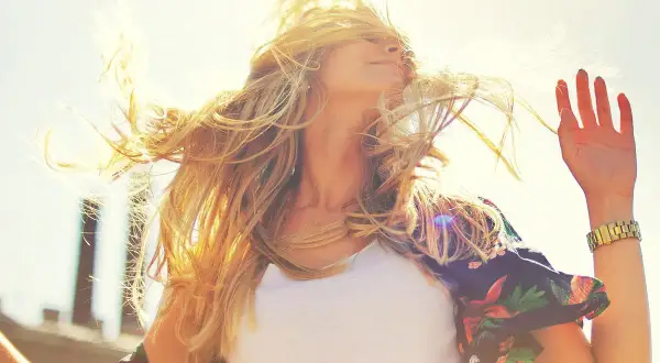 Une jeune femme aux cheveux blonds, illuminés par le soleil, danse joyeusement. Sa chevelure vole au vent, capturant la lumière dorée.