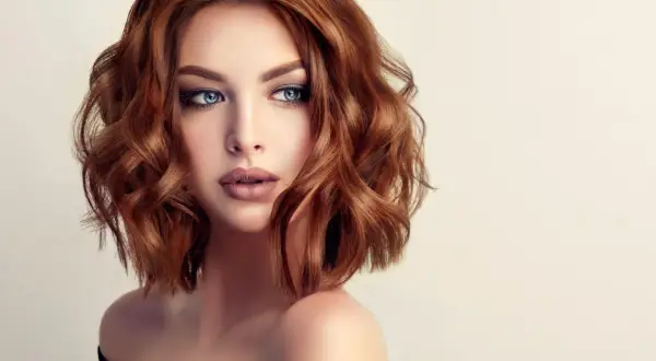 Une femme aux yeux bleus perçants et aux cheveux châtain clair ondulés, coiffés d'un brushing souple.