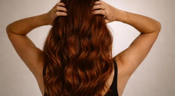 Vue arrière d'une femme aux cheveux ondulés d'une magnifique couleur cheveux auburn, ses mains dans sa chevelure.