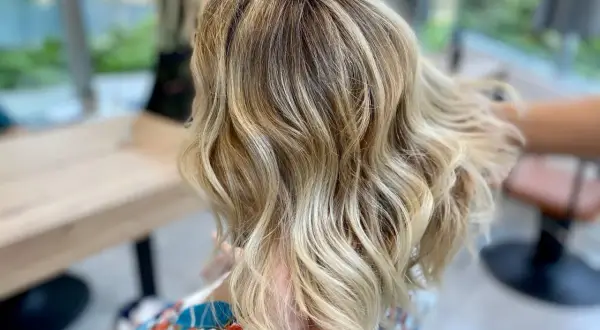 Chevelure blonde ondulée, parfaite pour comment cacher ses cheveux blancs. Les reflets subtils camouflent les premières mèches grises.