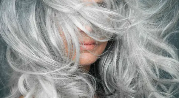 Gros plan sur une femme aux cheveux poivre et sel naturels, une chevelure argentée et volumineuse qui encadre son visage.