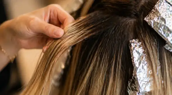Main d'une coiffeuse travaillant sur des mèches de cheveux, comparant le foilyage et le balayage pour un effet naturel.