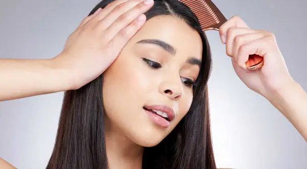 Une femme se peigne les cheveux, montrant comment enlever une raie de cheveux pour un look parfait.