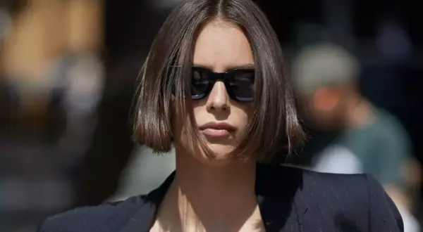 Une femme porte des lunettes de soleil et une veste, ses cheveux arborent une coupe carré court dégradé effilé.