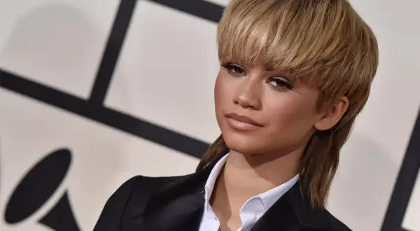 Zendaya arbore une coupe année 80 audacieuse, un mulet blond, avec un blazer noir et une chemise blanche.