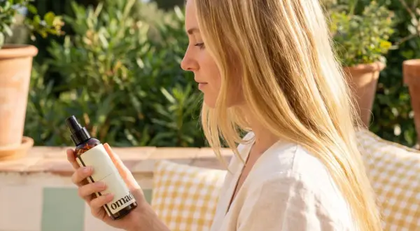 Une femme aux cheveux blonds tient un flacon. Elle cherche à éclaircir ses cheveux naturellement avec ce produit.
