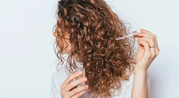 Une femme applique une huile sur ses cheveux bouclés pour définir ses frisottis.