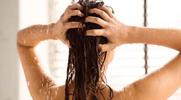 Une femme se lave les cheveux sous la douche, un moment de détente pour apprendre comment bien laver ses cheveux.
