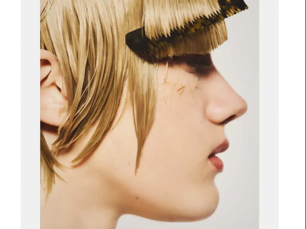 Une personne aux cheveux blonds mouillés, avec un peigne qui semble faire partie de sa frange, en pleine transformation.