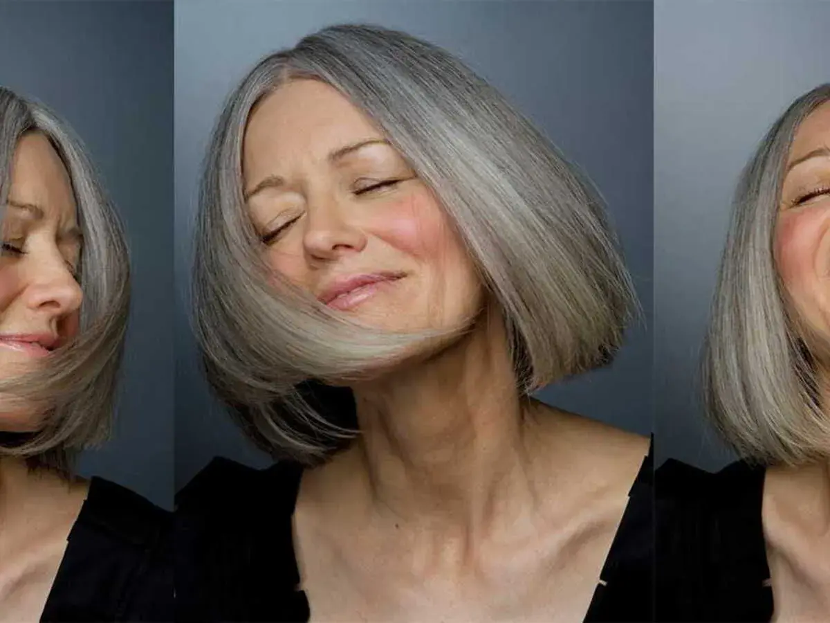 Une femme de 60 ans au visage ovale arbore une coupe de cheveux courte et grisonnante, exprimant joie et sérénité.