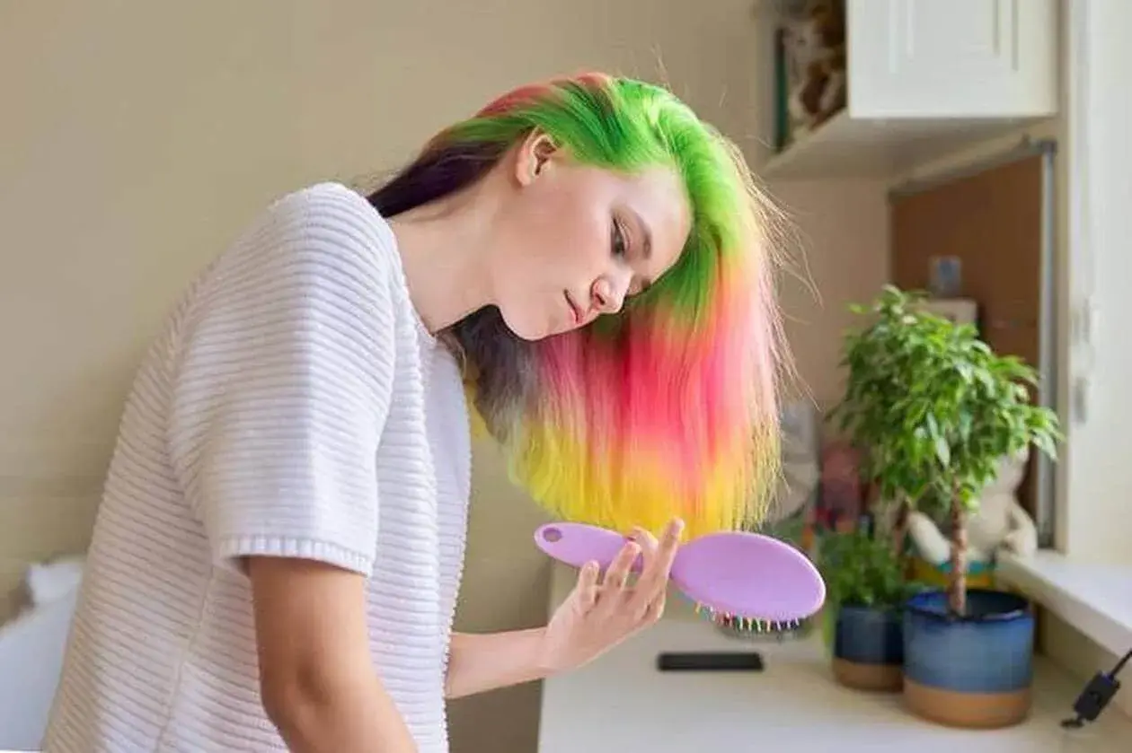 Jeune femme aux cheveux multicolores, elle se prépare à refaire une couleur par-dessus une couleur, avec une brosse à la main.
