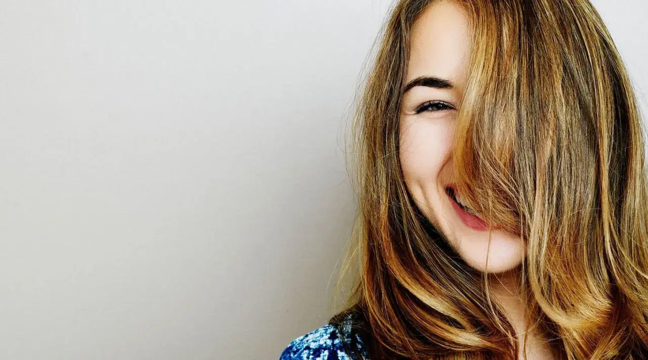 Une jeune femme rit, ses cheveux eclaircis tombant sur son visage.