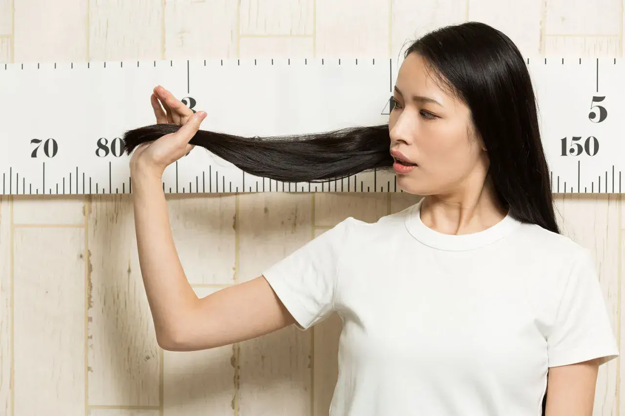 Femme mesurant sa longue chevelure noire devant une règle graduée, peut-être pour suivre le ralentir pousse cheveux.