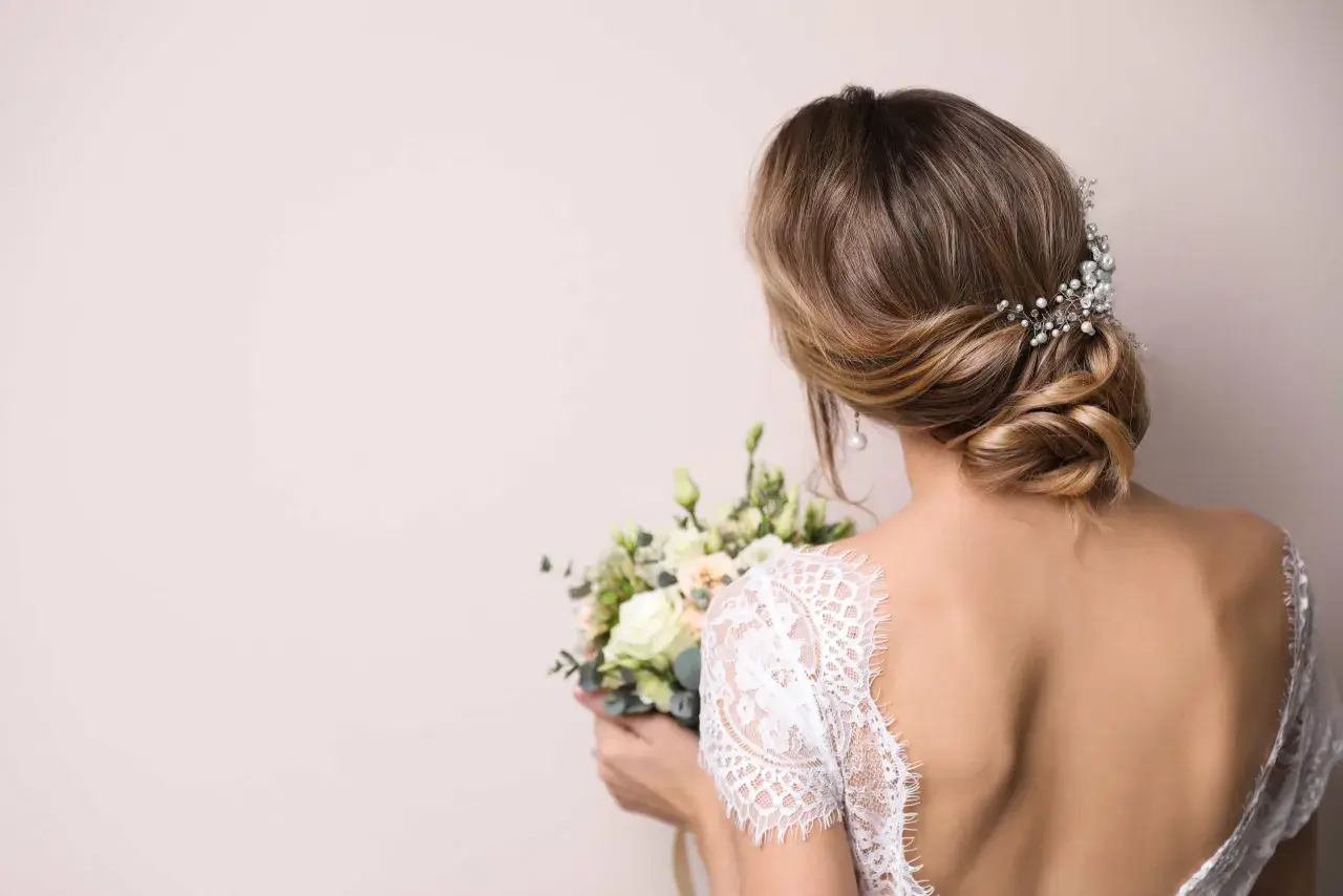 Coiffure bohème chic mi long avec un chignon bas orné de perles et de cristaux, tenant un bouquet de mariée.