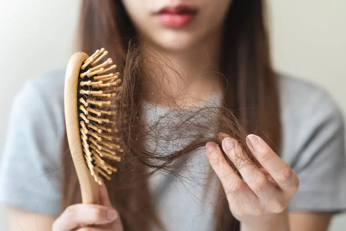 Une femme examine sa brosse à cheveux, remplie de mèches, signe de cheveux cassants.