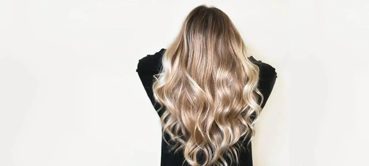 Cheveux châtain transformés en une cascade de mèches blondes lumineuses, un éclaircissement subtil pour un look naturel et ensoleillé.