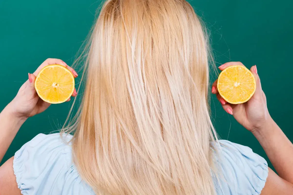 Une femme aux cheveux blonds tient des moitiés de citron près de ses oreilles, suggérant des aliments mauvais pour les cheveux.