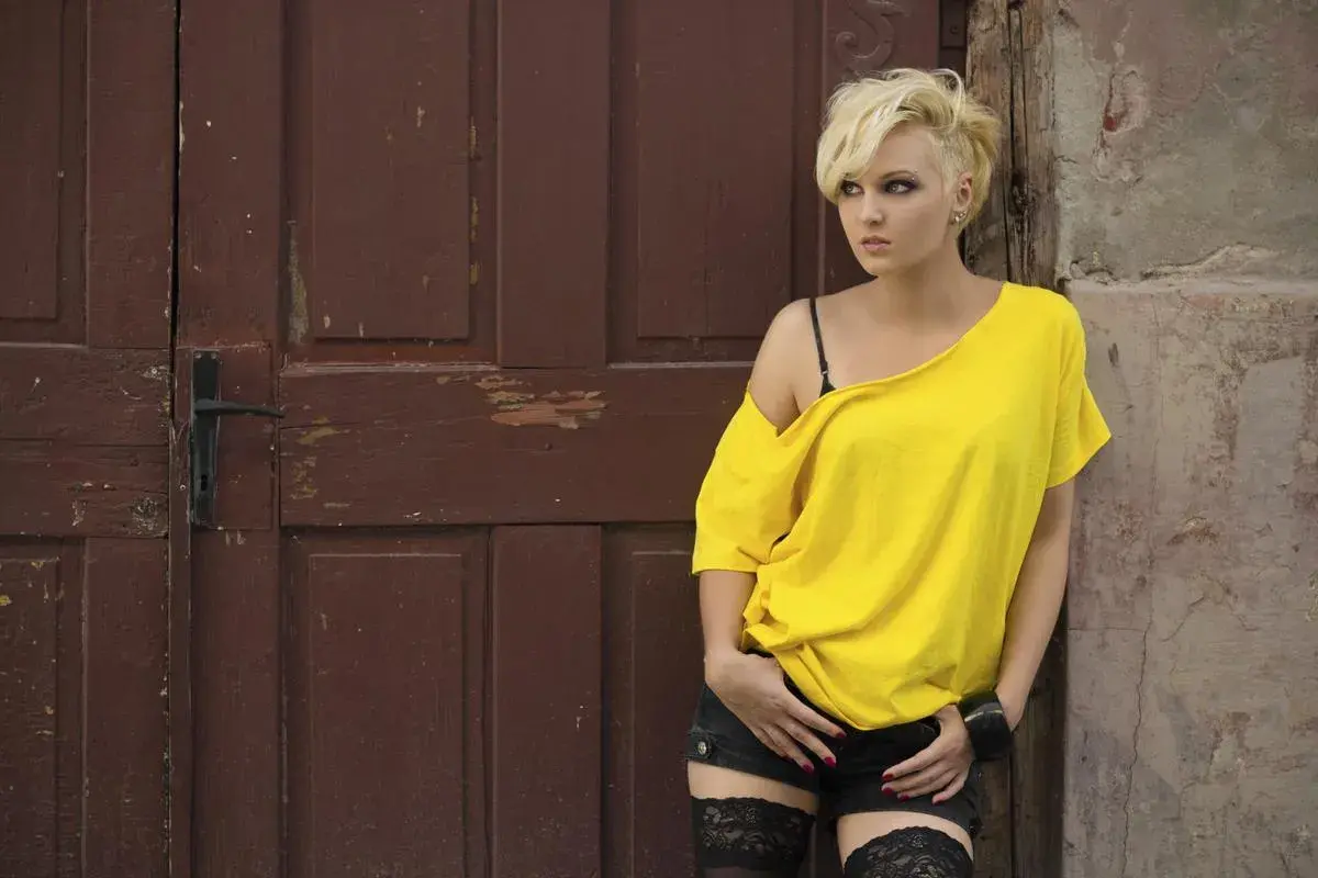 Jeune femme au look rock chic, coupe courte blonde, t-shirt jaune dénudant une épaule, short noir et bas résille.