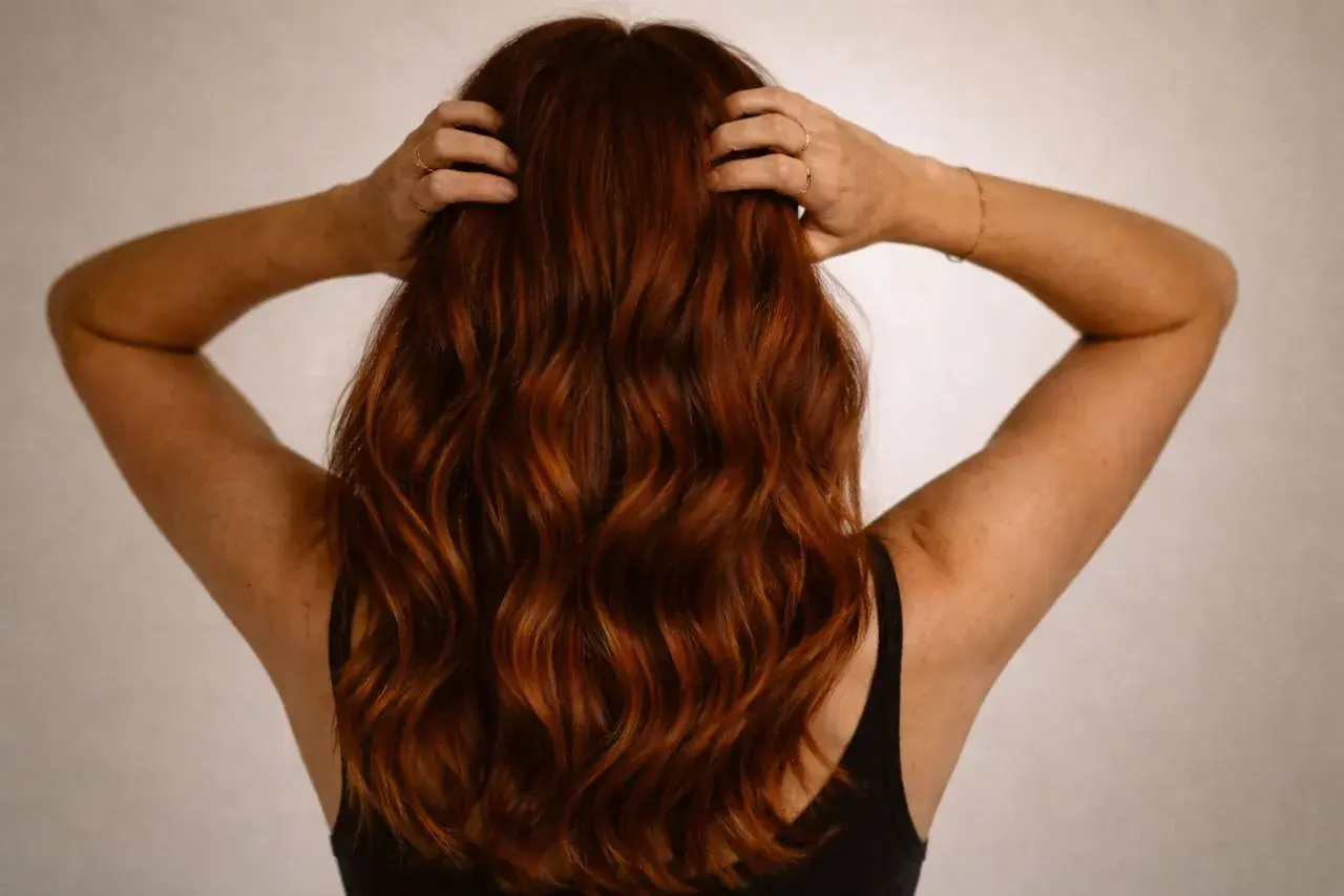 Vue arrière d'une femme aux cheveux ondulés d'une magnifique couleur cheveux auburn, ses mains dans sa chevelure.