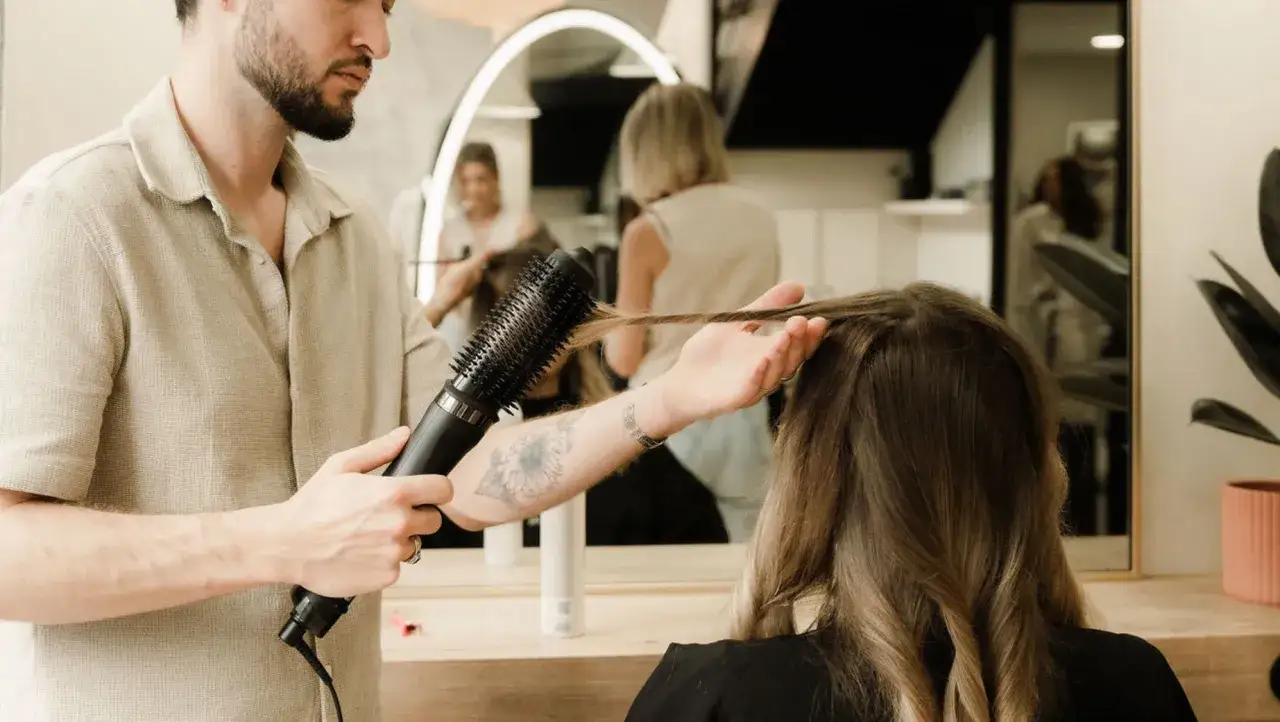 Coiffeur utilisant un sèche-cheveux et une brosse pour obtenir des cheveux brillants comme chez le coiffeur.