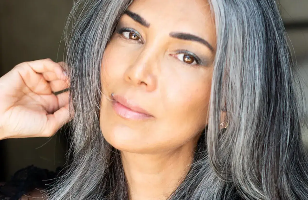 Une femme au carré cheveux gris dégradé, la main effleurant une mèche. Son regard est intense, souligné par un maquillage subtil.