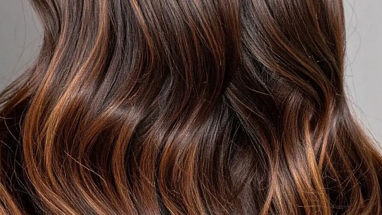 Chevelure brune aux reflets chauds, un balayage dégradé subtil qui illumine les ondulations naturelles.