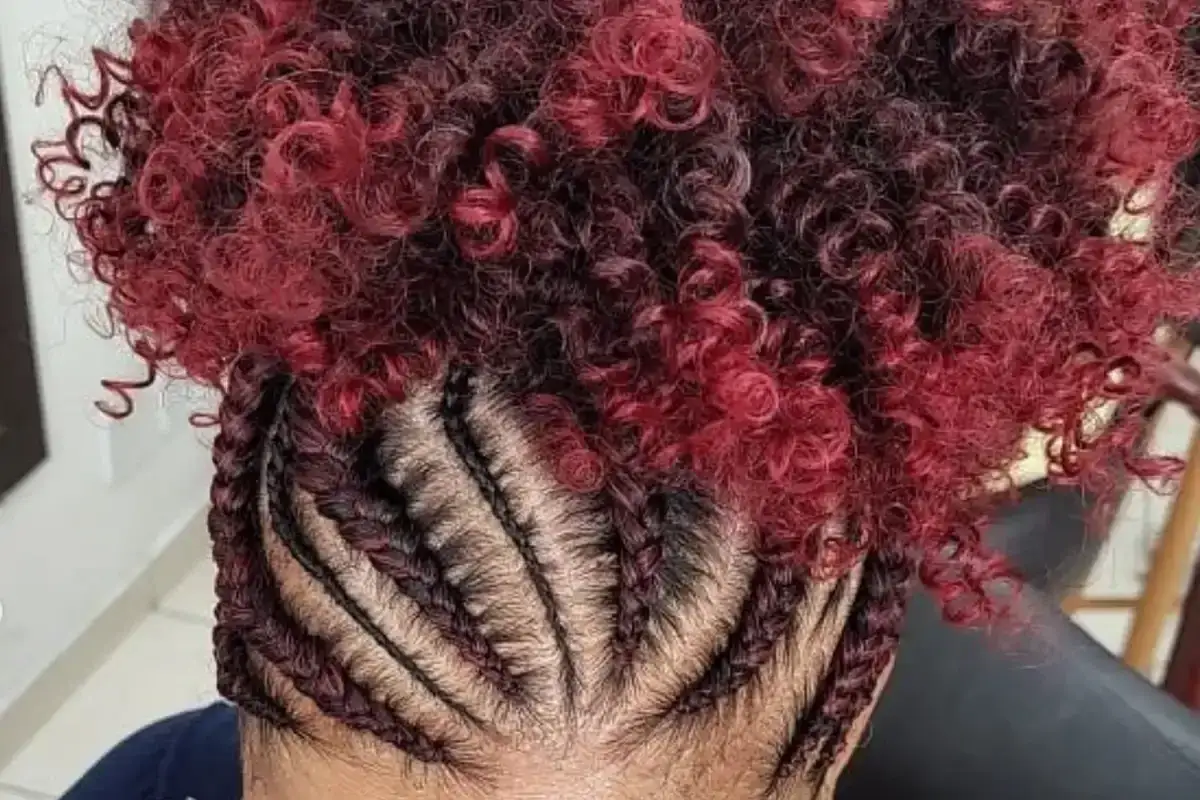 Une coiffure audacieuse avec des tresses sur le devant et une explosion de cheveux boucl&eacute;s rouge et noirs sur le dessus.