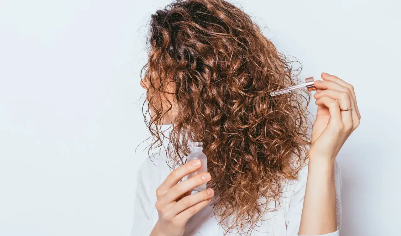 Une femme applique une huile sur ses cheveux boucl&eacute;s pour lutter contre les cheveux cassants.