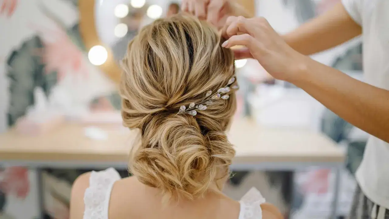 Une mari&eacute;e se fait coiffer un chignon boucl&eacute; flou, orn&eacute; d'une barrette scintillante.