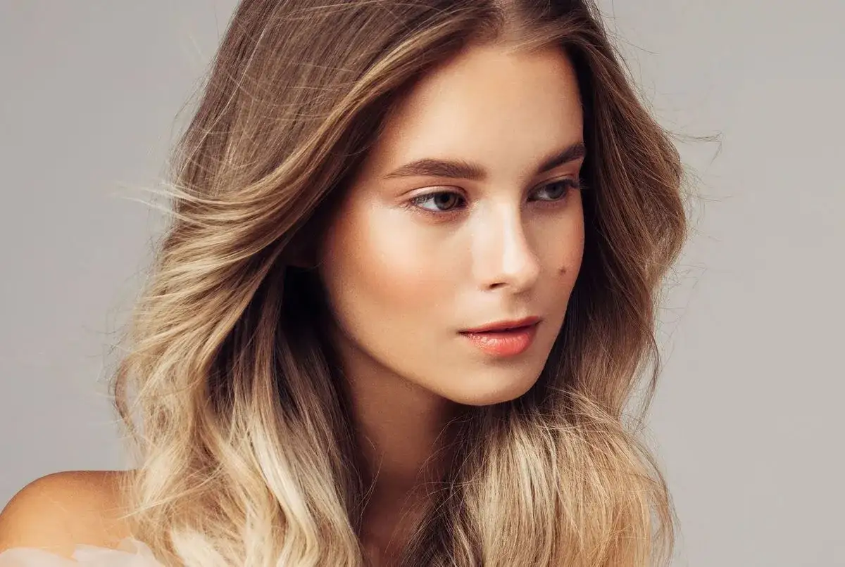 Une jeune femme avec de magnifiques cheveux eclaircis, ondul&eacute;s et brillants, sur fond gris.